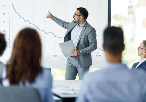 Young male leader giving his colleagues a presentation about economic depression in the office.